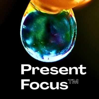 Photo of a transparent green and blue sphere hanging from an orange banner, against a black background with white text that reads, ¨Present Focus¨