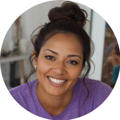 Cropped circle photo of a lovely woman with brown skin, nice smile, her hair in a bun on her head, wearing a purple T-shirt in an art studio.
