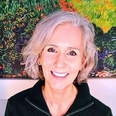 photo of Maya Frost, founder of Collapse Forward, smiling, wearing a green half-zip sweater in front of a a colorful Van Gogh painting.