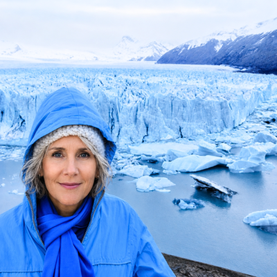 photo of Maya Frost, human adaptation and resilience expert, standing in front of a glacier in Calafate, Argentina, wearing a blue jacket and scarf