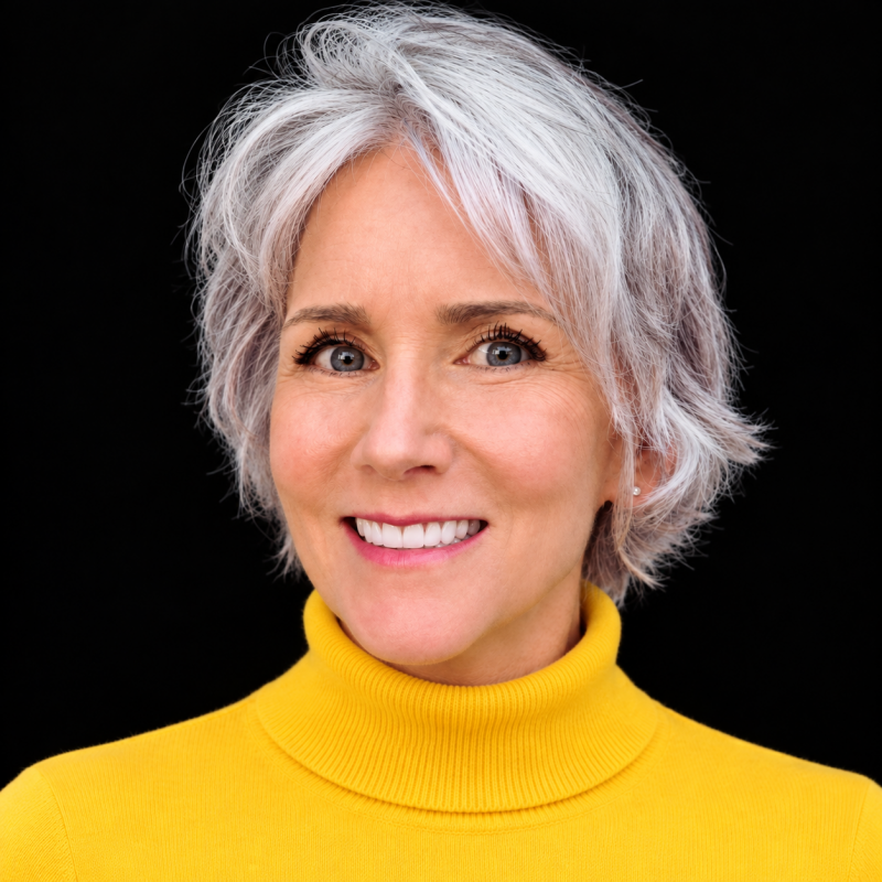 Professional headshot of Maya Frost, founder of Collapse Forward, creator of Lucid Longing, wearing a yellow turtleneck, black background