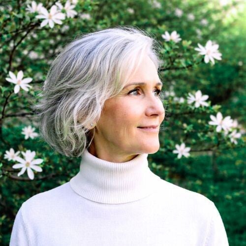 Maya Frost, founder of Collapse Forward, wearing a white turtleneck sweater, standing in front of blooming spring tree.