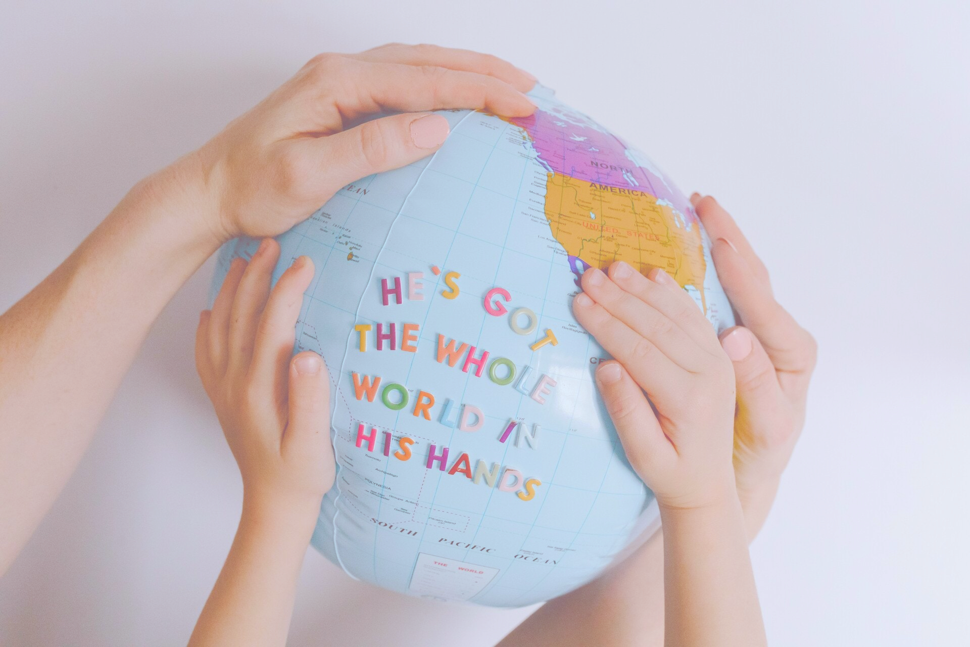 Äiti ja lapsi pitävät maapalloa käsissään, jossa lukee "He's got the whole world in his hands" – Omakätilö tarjoaa suomenkielistä kätilön tukea kaikkialle maailmaan