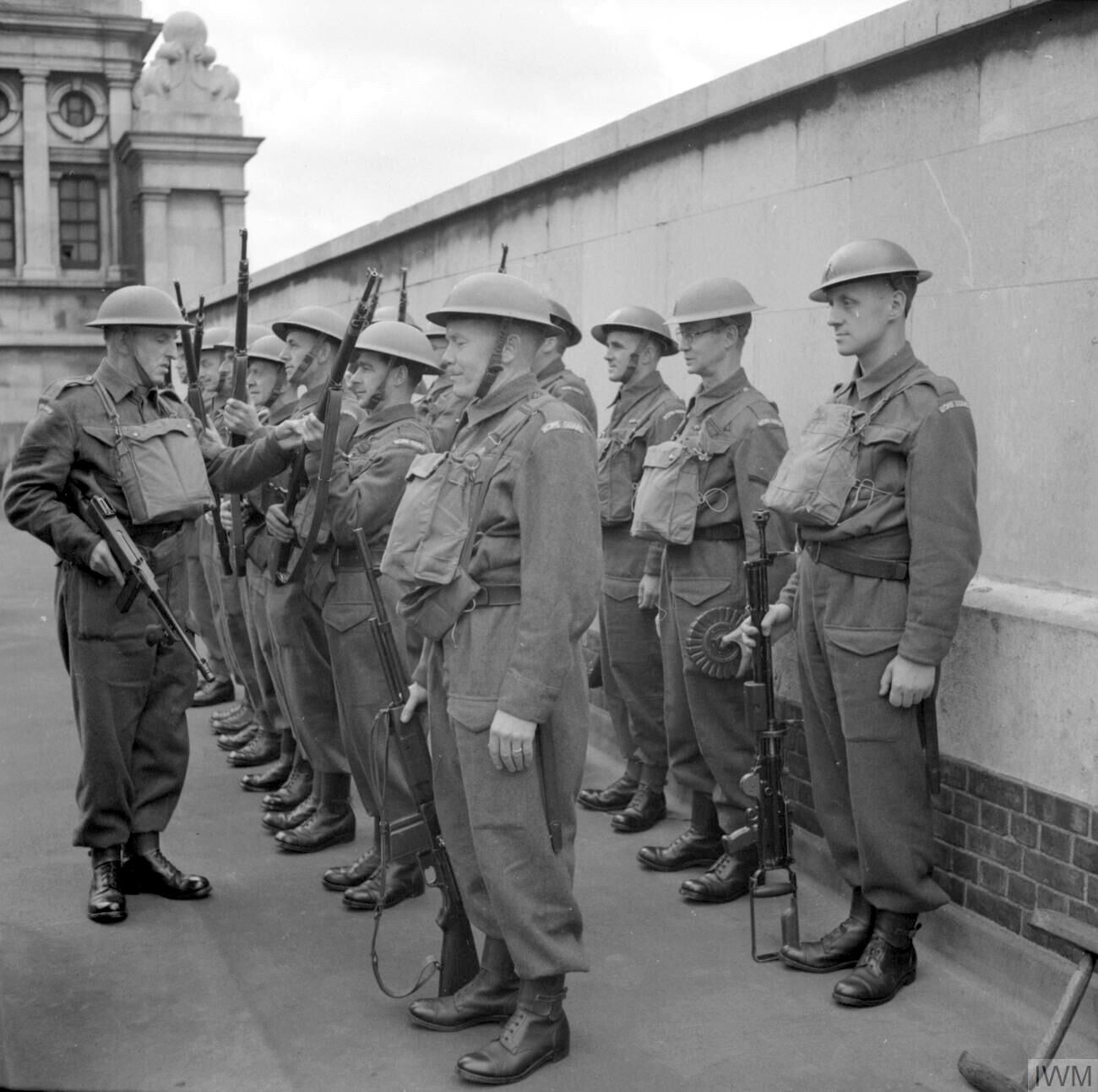 British Home Guard soldiers lined up for weapon inspection during the Second World War, carrying Lee-Enfield rifles and wearing standard Home Guard uniform.