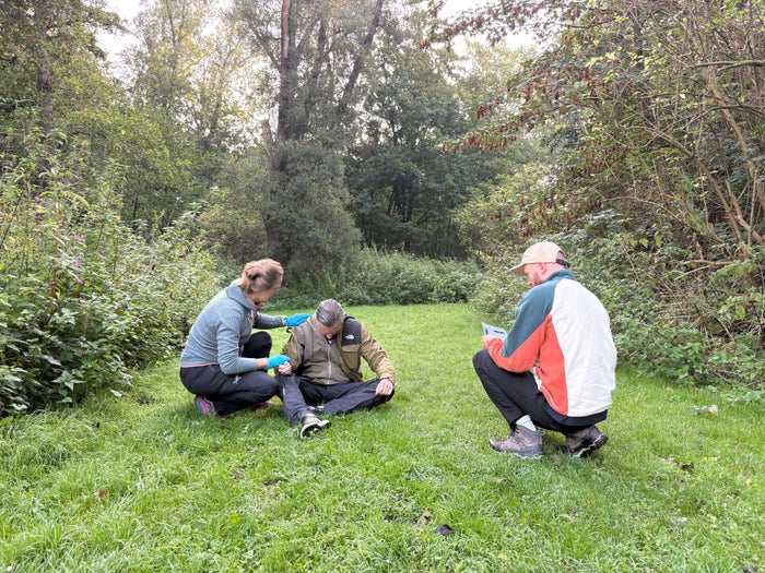 Deelnemers oefenen een scenario tussen de bomen tijdens EHBO in de wildernis