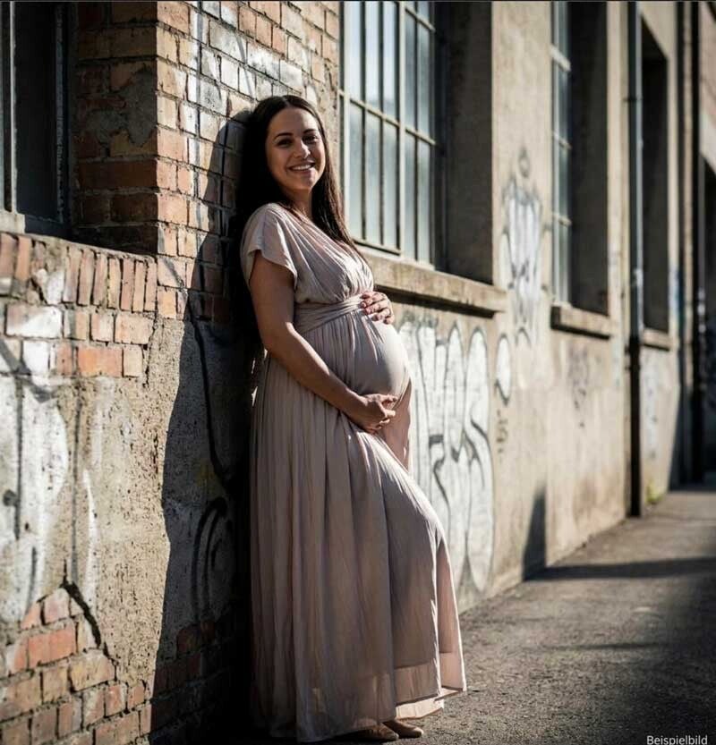 Schwangere Frau in einem stilvollen, fliessenden Kleid, das ihren Bauch betont, auf dem Viscosistadt-Areal in Emmenbrücke. Sie steht vor einer Wand mit dezentem Graffiti, umgeben von der charakteristischen Industriearchitektur.