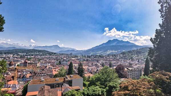 Weite Panorama-Aussicht von der Museggmauer über die Dächer der Luzerner Altstadt mit den Schweizer Alpen und dem Pilatus im Hintergrund.
