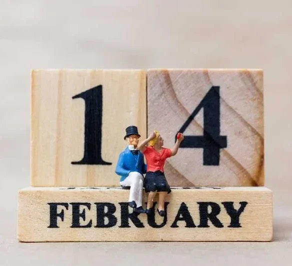 Miniaturfiguren eines Paares auf einem Holzkalender, der den 14. Februar zeigt.