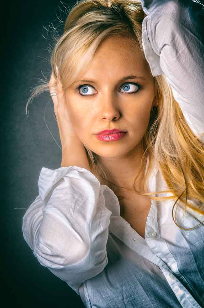 Nahaufnahme einer blonden Frau in weißer Bluse, die mit grossen Augen zur Seite blickt