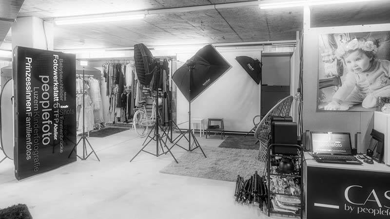 Grosszügiger Aufnahmebereich des Studios mit Scheinwerfern, weissem Hintergrund und einem Arbeitsplatz mit Laptop.
