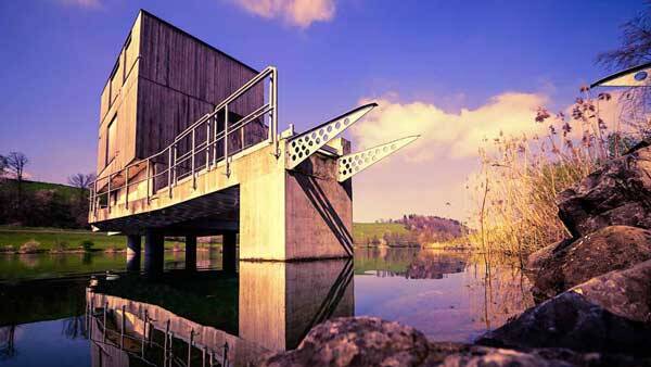 Das markante Starthaus der Ruderregatta auf dem Rotsee – ein moderner Holz- und Betonbau auf Stelzen, der sich bei atmosphärischem Licht im stillen Wasser spiegelt.