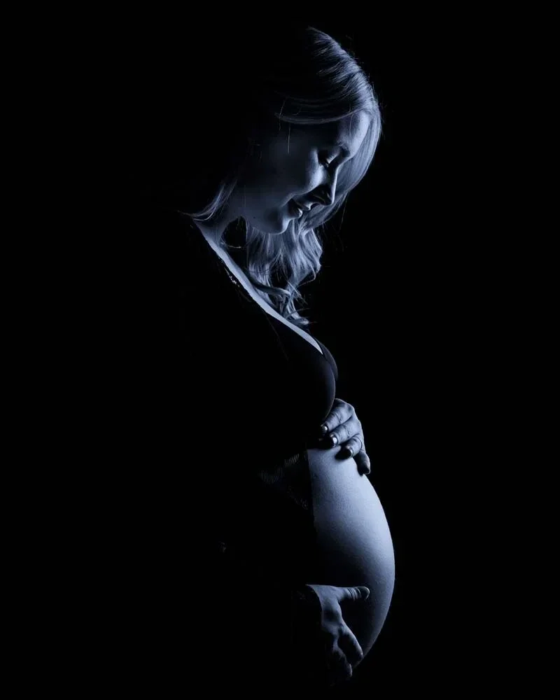 Kunstvolles Low-Key-Silhouette-Portrait eines Schwangerschaftsbauchs, dramatische Beleuchtung im Dunkeln.