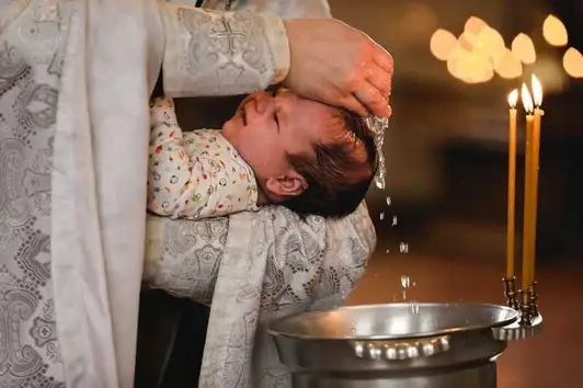 Ein stimmungsvolles Foto von einem Tauf-Fotoshooting in Luzern: Ein Pfarrer giesst Wasser über den Kopf eines Babys.