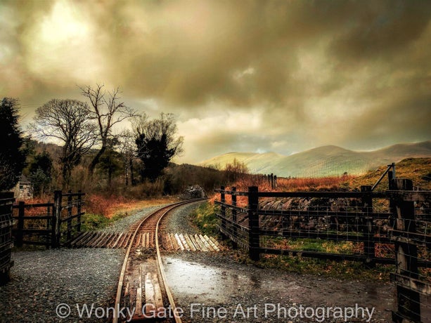 Photograph of railway crossing in stormy weather with mountains in background.