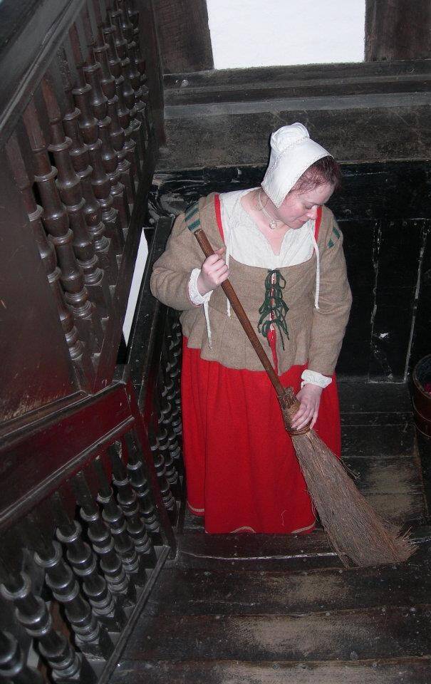 Woman wearing 17th Century clothing sweeping a wooden staircase