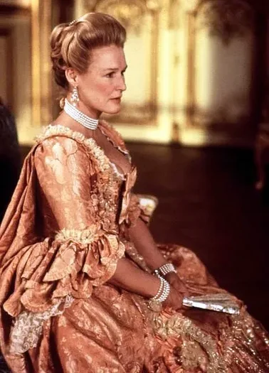 Photo of a seated woman with fair hair wearing a peach damask 18th Century gown. She also wears a multi stranded pearl choker, and matching bracelets and holds a folding fan