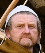 Photo of a man's head with sandy red hair and beard, wearing a small white cap with ties under the chin