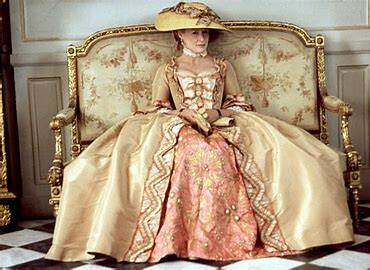 Photo of a woman sitting on a settee wearing an 18th Century gown made from buff coloured taffeta, with a darker peach brocade petticoat. She also wears a wide brimmed straw hat