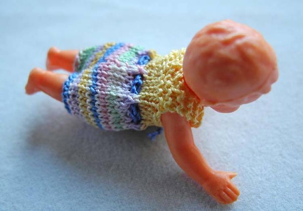 Plastic popje, buikligging, geel en veelkleurig pakje - Plastic doll, laying on its belly, yellow-multi colour suit