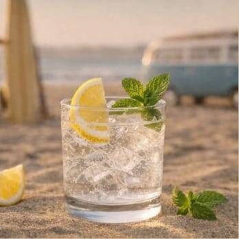 Koyi Gin Tonic am Strand mit VW Bus und Surfboard im Hintergrund