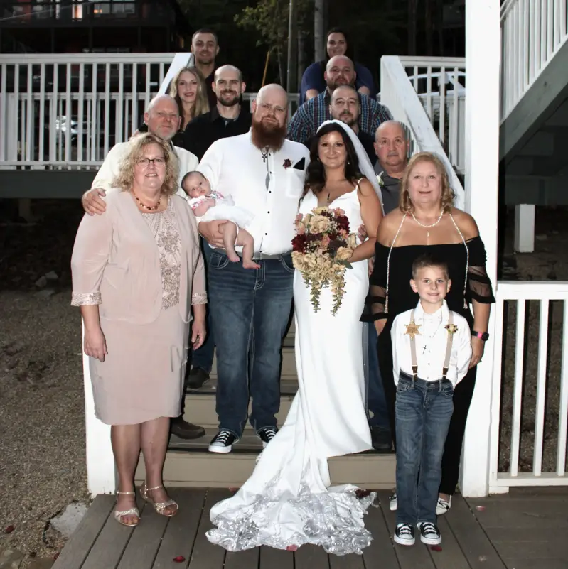 large-family-wedding-portrait-on-outdoor-cabin-stairs-featuring-a-bride-with-bouquet-groom-holding-a-baby-and-guests-in-the-great-smoky-mountains-standard-wbhv4u.webp