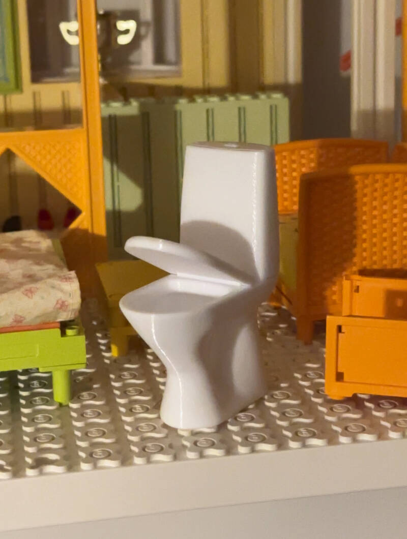 1:10 WC-istuin nukkekotiin. Mallinnettu itse ja tulostettu PETG-muovista. Saranalla liikkuva kansi.