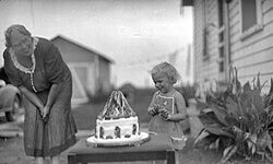 “A child standing beside a Snow White‑themed birthday cake in an early 1900s photograph, with their mother nearby, capturing a vintage celebration moment.”