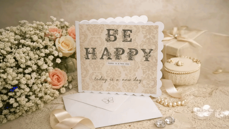 Vintage‑style birthday card with gold “Be Happy” lettering and falling petals on a cream envelope.