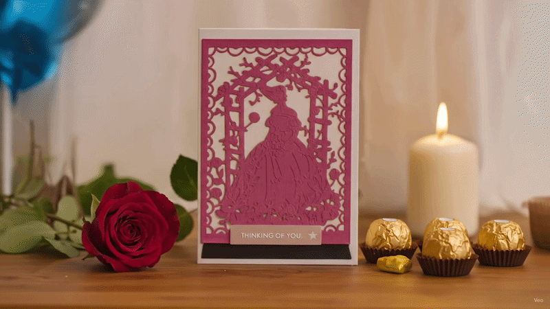 Handmade Valentine card with pink cutout design, red rose, candle, and gold chocolates, displayed in a warm romantic setting.