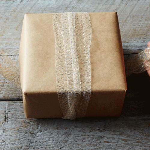 🎁 Hands tying a glittery ribbon around a wrapped gift box.