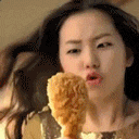 A young woman gazing eagerly at a box of crispy chicken drumsticks, smiling with a playful, tempted expression.