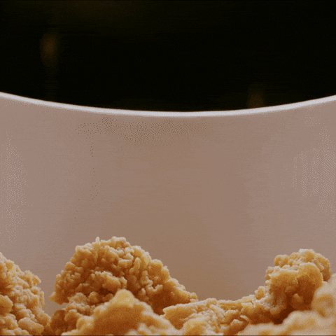 Golden chicken drumsticks dropping into a serving box in a fun looping animation, creating a lively, appetising moment.