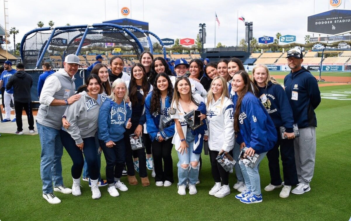 Softball team at the Dodgers game smiling all together on the field. 