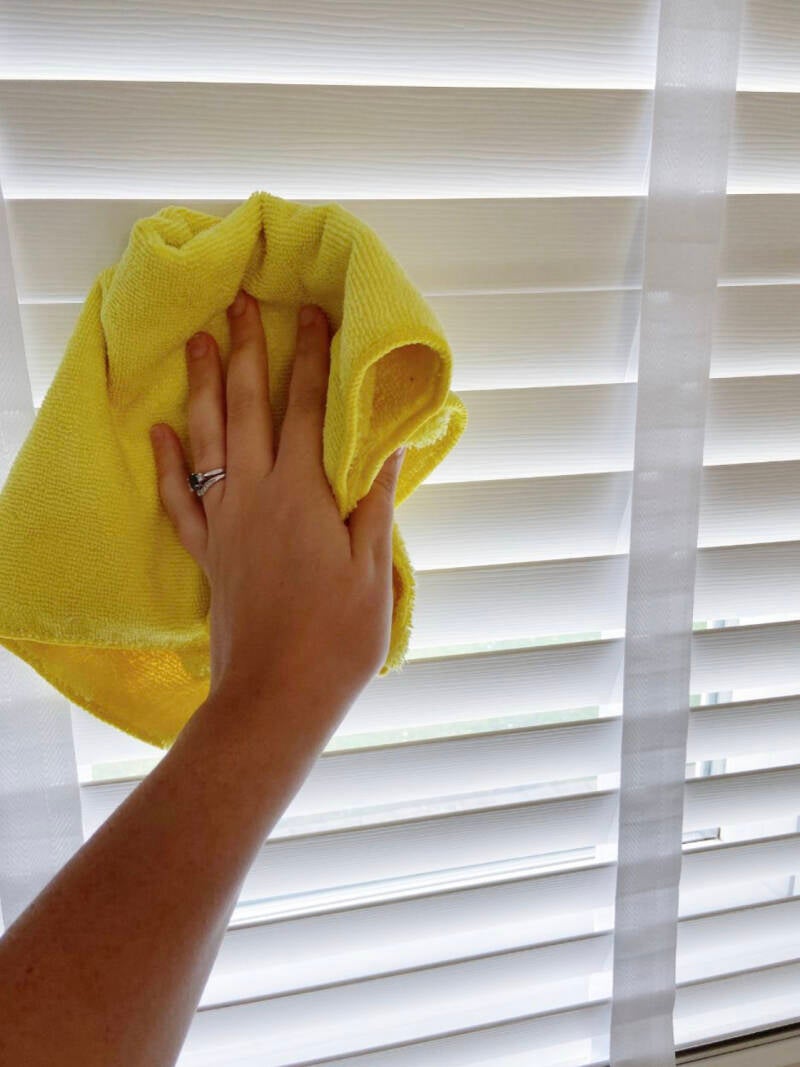 Cleaning wooden blinds with a yellow cloth