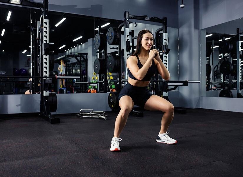 Femme faisant des squats en salle de sport pour développer sa masse musculaire et accélérer son métabolisme