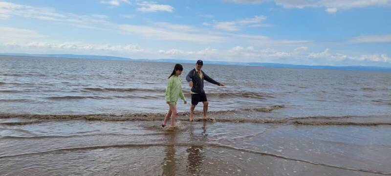 Two young people dip their toes in shallow water at the beach