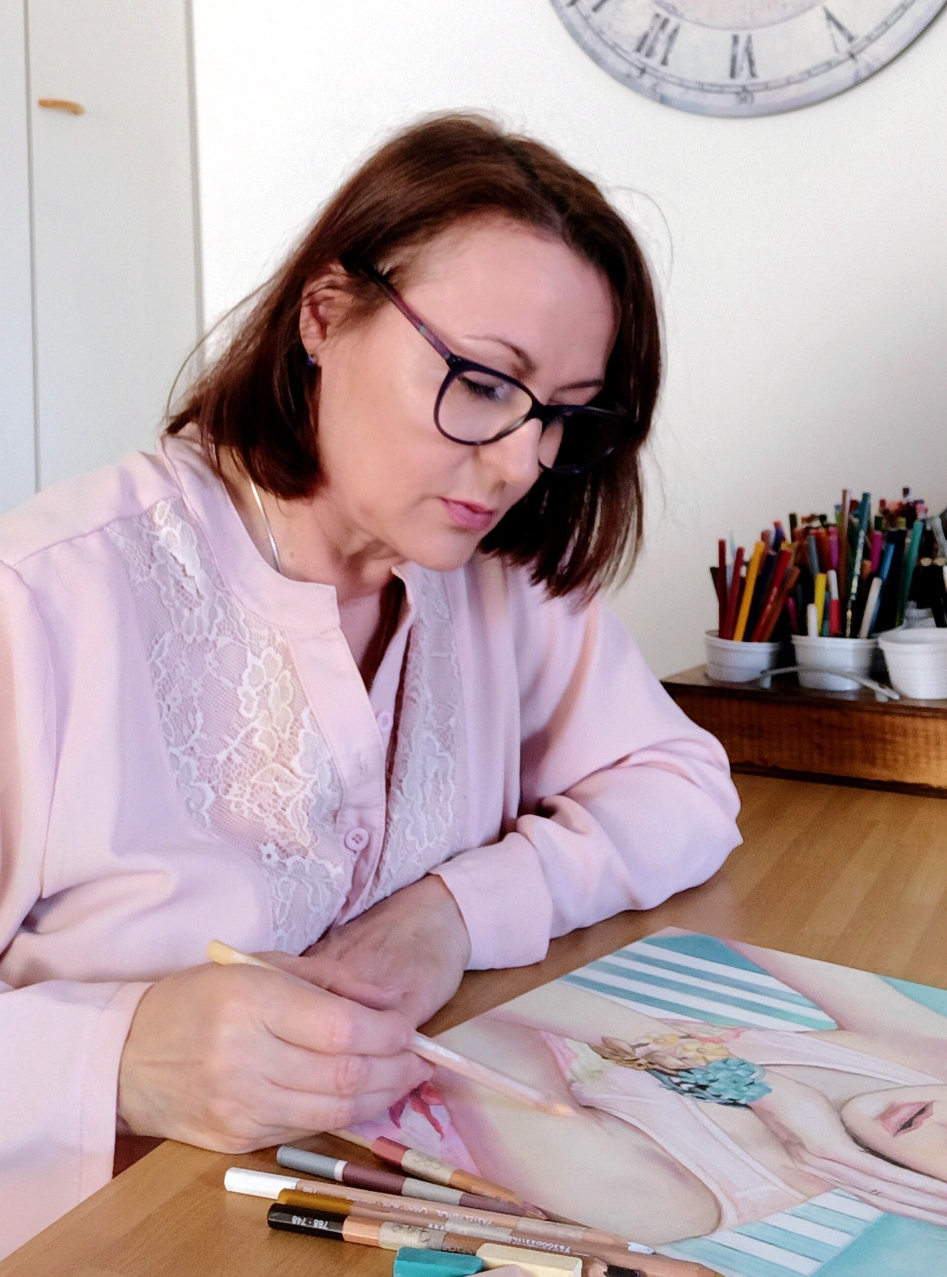 Eleonora Sgura pittrice di ritratti a pastello al lavoro nel suo atelier a Turate - artista con occhiali che disegna ritratto femminile su commissione con matite pastello soft su tavolo in legno
