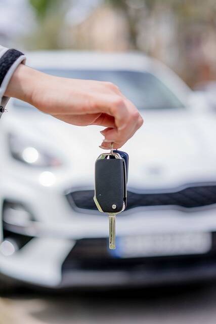 L'immagine di una chiave per auto in mano al nuovo proprietario con in sfondo la macchina nuova noleggiata