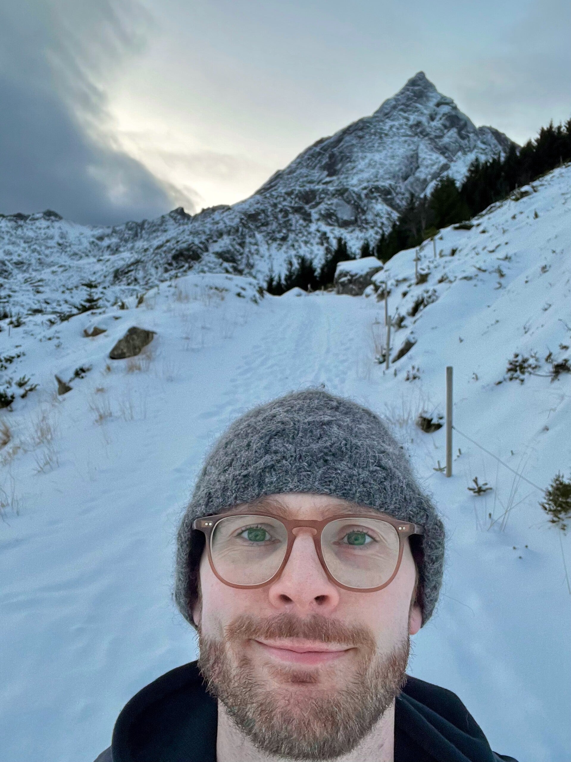 Bjorn in front of a wintery landscape in the Lofoten Islands, with the snow-covered mountain Skottinden in the background