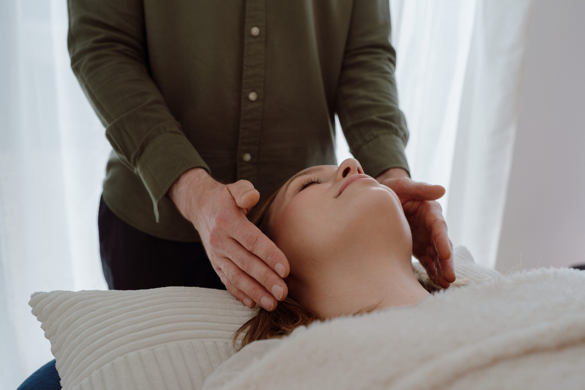 Hands resting lightly either side of a smiling client's head as she relaxes with her eyes closed on a treatment table