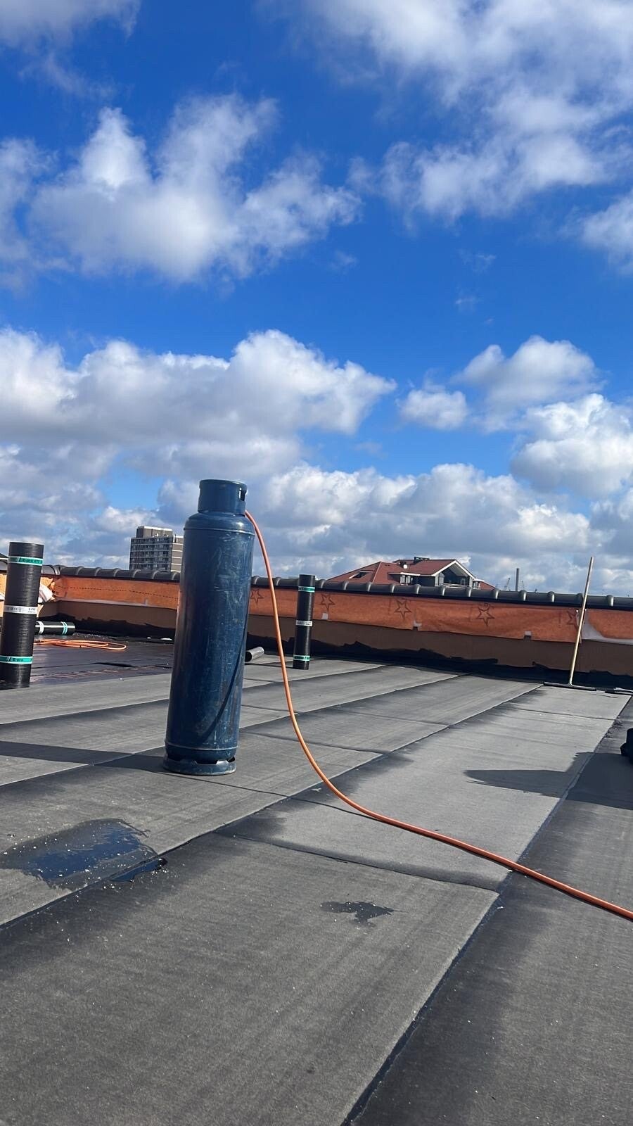 Nieuw gelegde bitumen dakbedekking op een plat dak, met gasfles en dakrollen van Dakwerken RVB