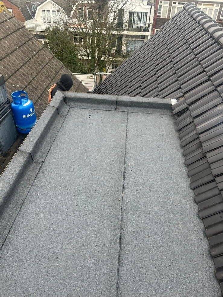 Dakdekker van Dakwerken RVB aan het werk bij een nieuw bitumen dak tussen pannendaken