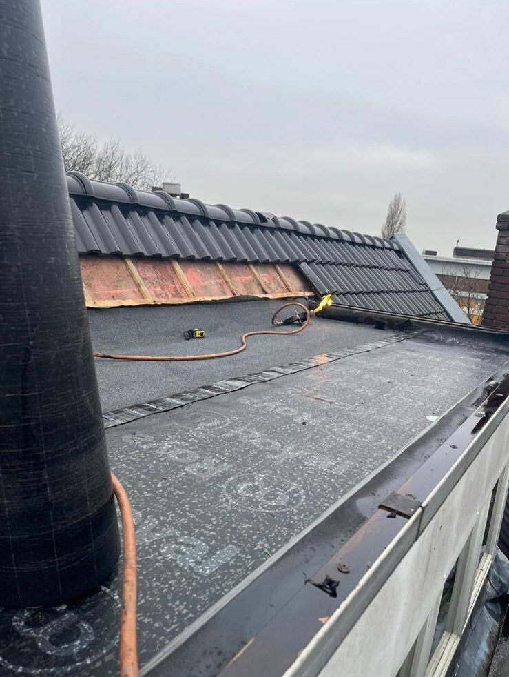 Dakdekkerswerk in uitvoering: bitumen wordt gebrand op een plat dak naast een pannendak