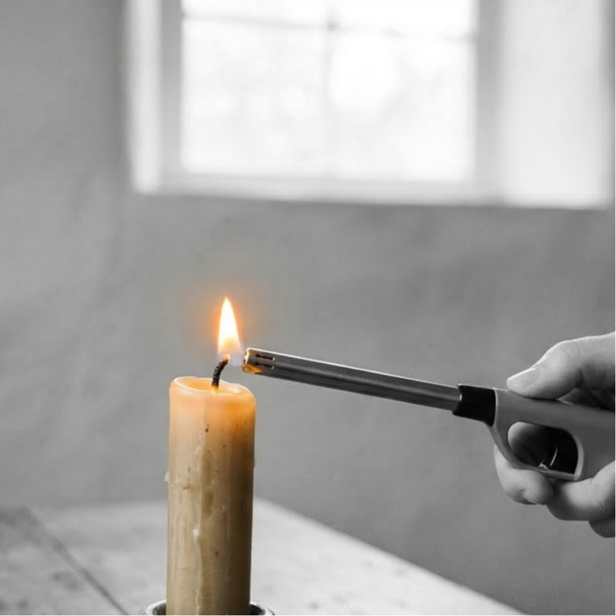 Zwart-wit foto van een hand in een gebreide trui die een lange aansteker vasthoudt bij de pit van een grote beige kaars op een rustieke houten tafel. Het enige gekleurde element is de vlam van de kaars, die levendig oranje en warm is.
