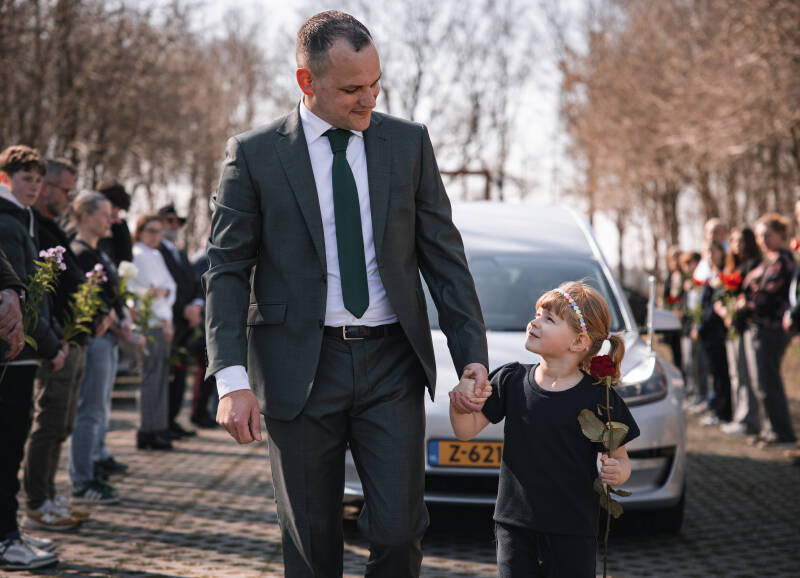 Uitvaartverzorger Vincent Hekert loopt hand in hand met een jong meisje met een roos.