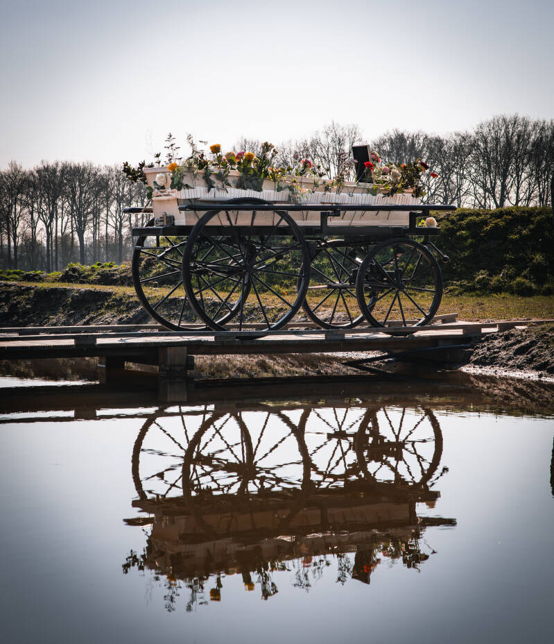 Een traditionele loopkoets met uitvaartkist weerspiegelt prachtig in het water.