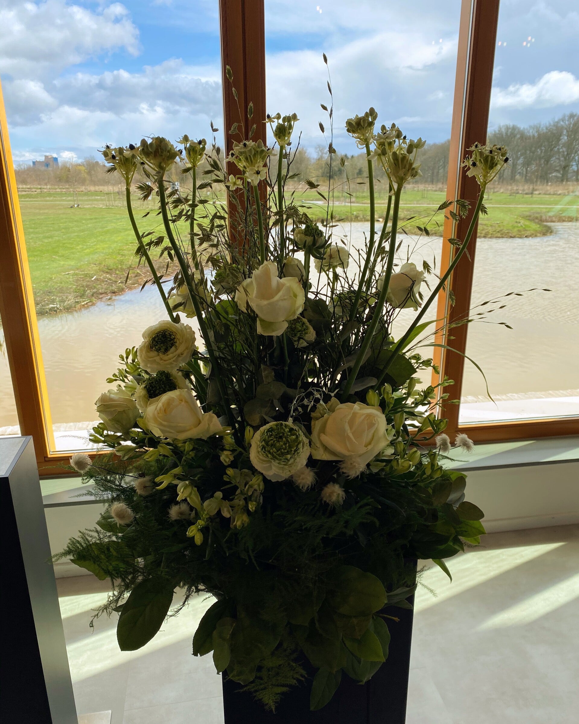 Uitvaartbloemen in aula, witte rozen in een bloemstuk. Hoog opgestoken. 