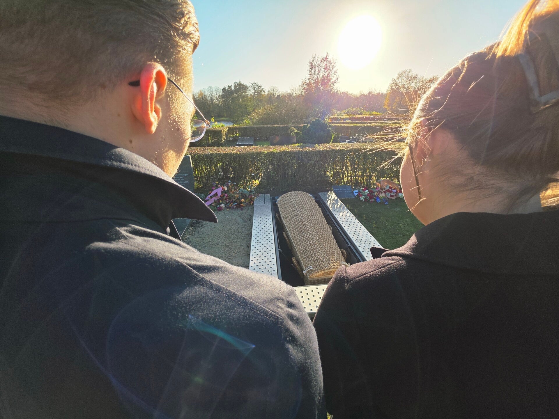 Een man en vrouw kijken in het heldere zonlicht samen uit over een begraafplaats.