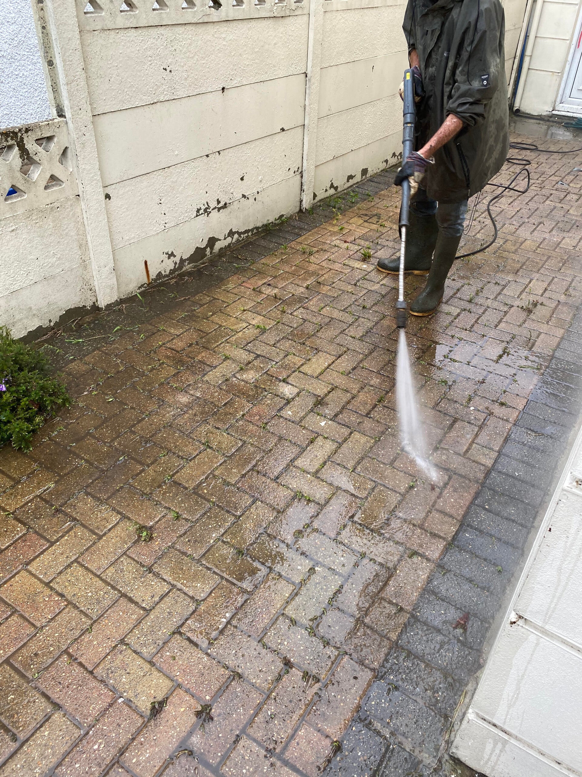 A professional pressure washing service cleaning a residential red brick driveway.