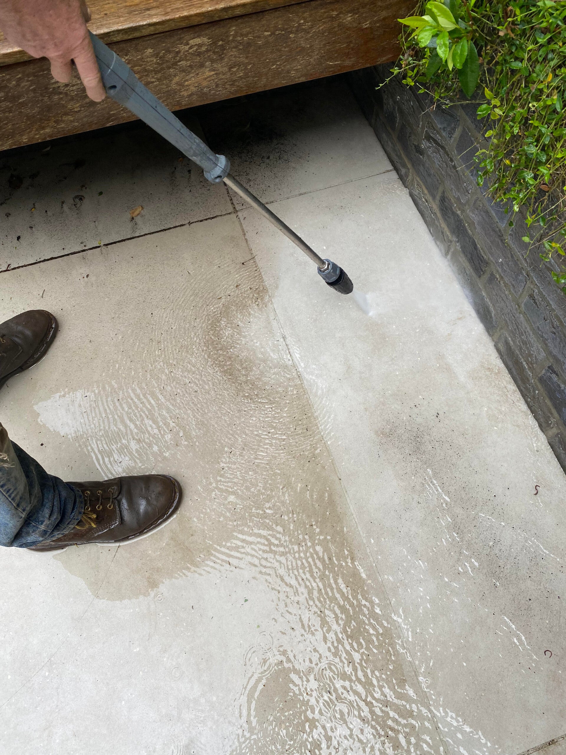 Person pressure washing a dirty outdoor patio with a high-pressure water wand.